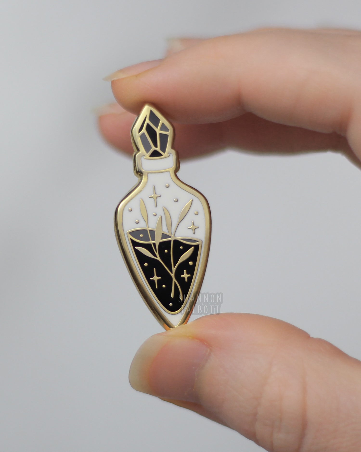 hand holding gold plated potion bottle enamel pin with plants